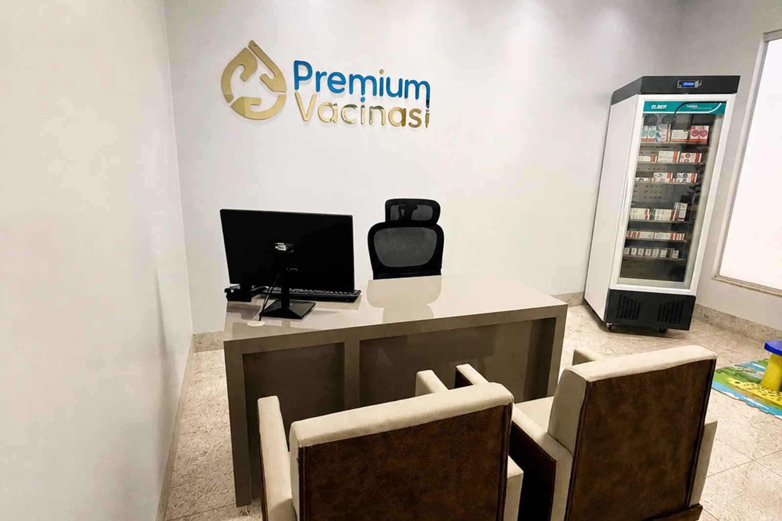 Sala de aplicação da Premium Vacinas, com identificação na parede, bancada de preparo e câmara de conservação