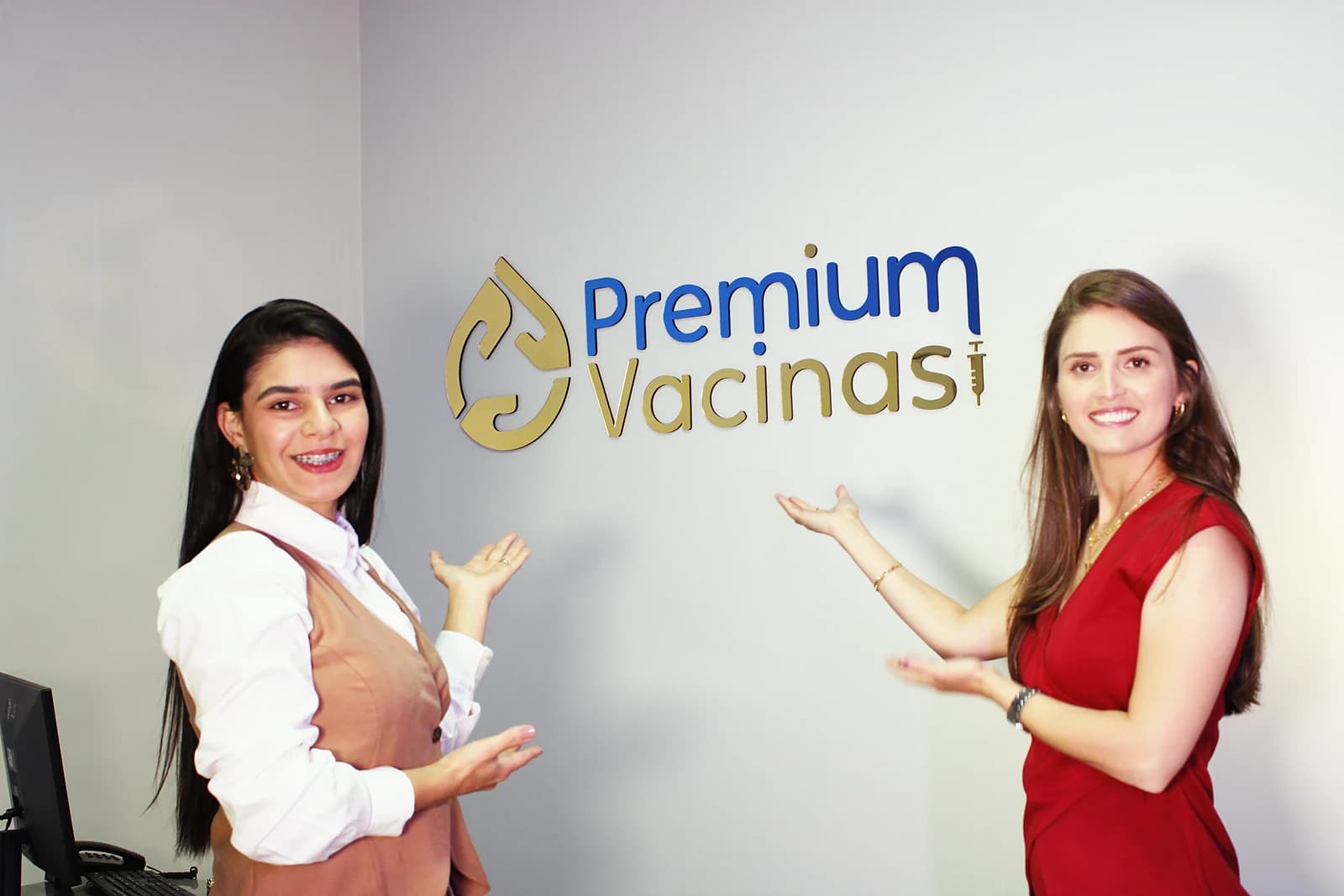 As sócias Myckaella Lima Pontes e Jeovana de Lima Cruz em frente ao logo da Premium Vacinas, na sala de vacinação